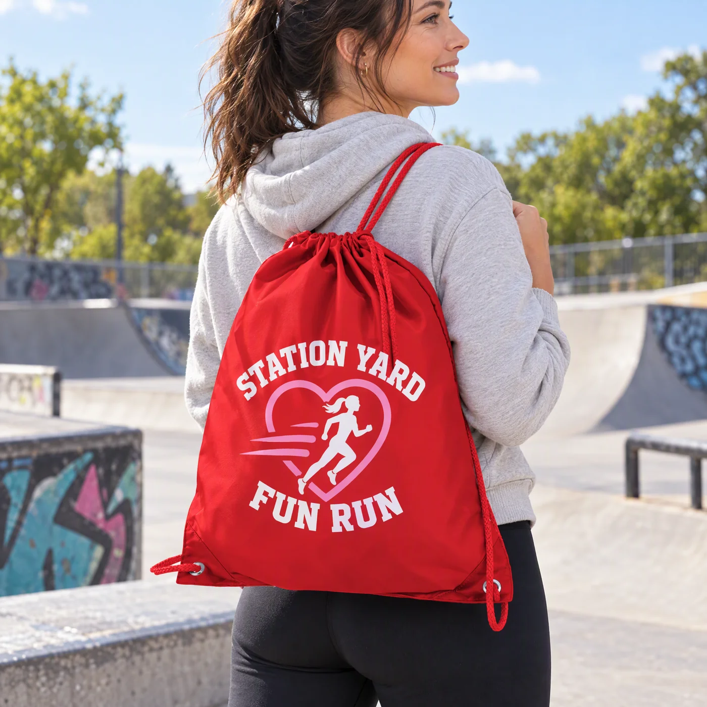 Woman in a skate park wearing a red polyester drawstring bag printed with a fun run logo