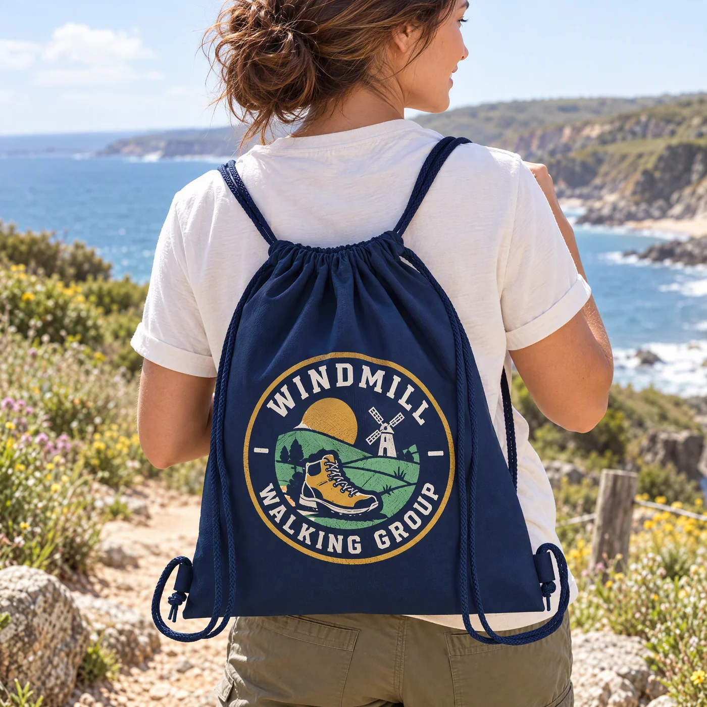 French navy cotton drawstring bag printed with a four-colour Windmill Walking Group logo, carried along a coastal path